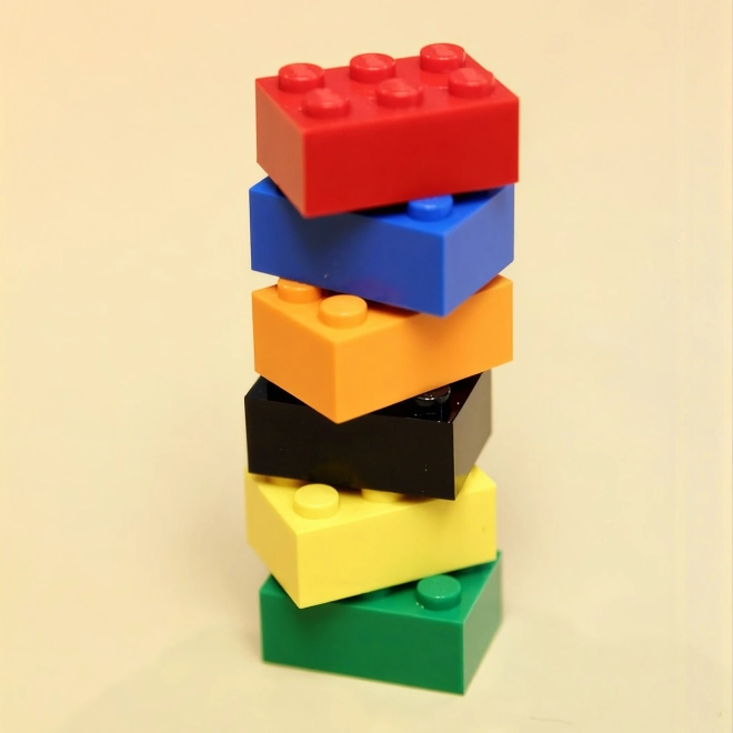 Seks fargerike LEGO-klosser stablet i en skjev tårn mot en lys bakgrunn